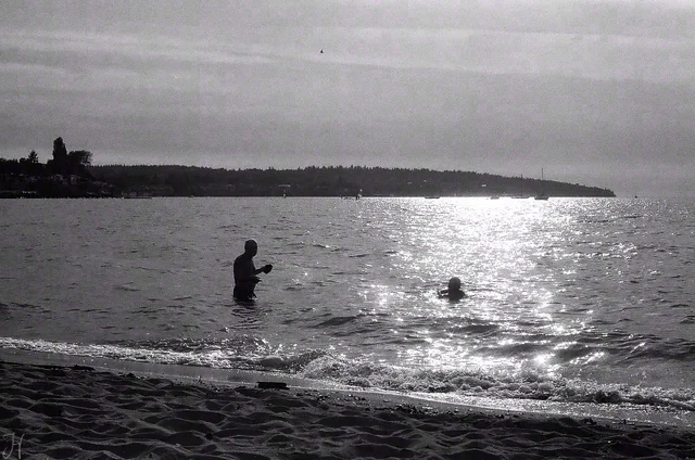 Black and white view of two people in shallow water beneath a wide patch of bright reflected sunlight.