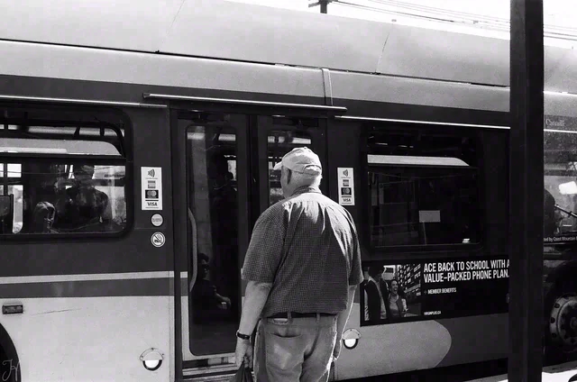 Black and white view of a person standing with their back to the camera beside an open bus door.