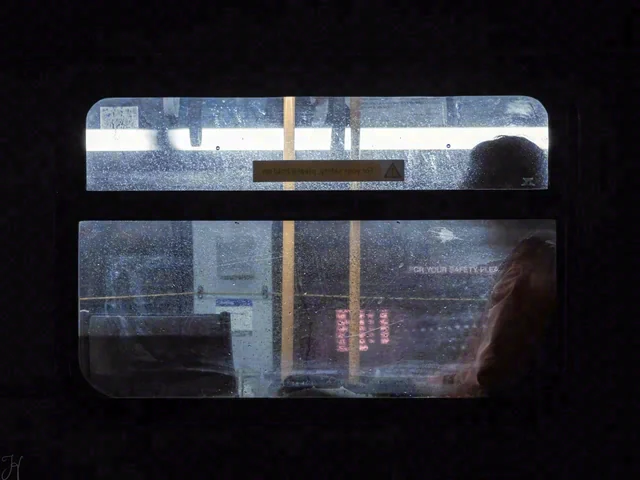 A dark interior frames a rain-speckled window and reflections, with part of a person visible on the right.